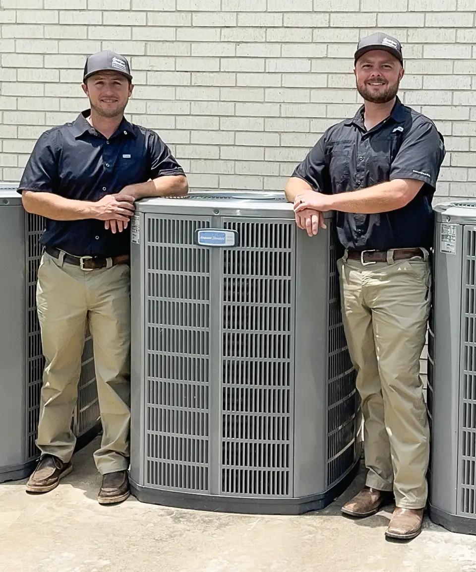Founders Dak and Clayton stand beside a high efficiency American Standard Air Conditioner.